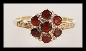 A stamped 9ct gold ring having a flower head set with seven round garnet stones. Weight 2.1g. Size