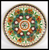 A 20th Century brass wall charger plate with enamelled geometric detailing in red and green hues.