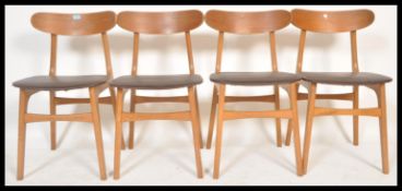 A set of four mid century 1970's teak wood dining chairs being raised on angular legs with pad seats
