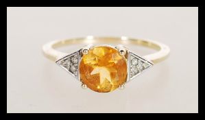 A hallmarked 9ct gold ladies ring set with a brilliant cut orange stone with triangular shoulders