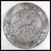 A 20th Century pewter wall charger having a raised scene of a fox in woodland with a bird flying