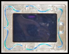 A 20th Century Tiffany style easel back photo frame having a silver frame with enamelled Art Nouveau