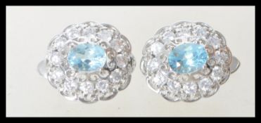 A pair of ladies silver dress earrings prong set with oval cut blue topaz stones with a halo of cz's