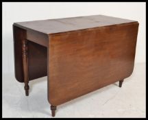 A 19th century mahogany George III drop leaf dining table being raised on turned, tapering legs with