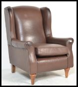 A contemporary brown leather wing back fireside armchair with scroll arms and loose seat pad