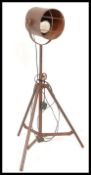 A vintage industrial floor standing adjustable spot light, raised on a metal tubular tripod frame.