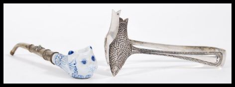 A pair of silver plated sugar tongs in the form of two fish along with a silver plated pipe with