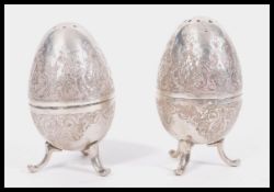 A pair of early 20th Century Arabic silver condiments pepperettes in the form of eggs raised om