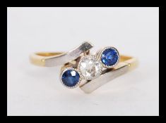 A stamped 18ct gold crossover ring millegrain set with a central diamond flanked by two round cut