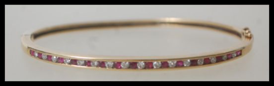A 9ct 375 stamped bangle bracelet having a pave set alternating line of rubies and diamonds. The