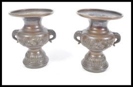 A pair of 19th Century Chinese bronze vases raised on circular pedestal bases with twin elephant