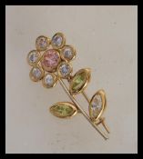 A stamped 750 18ct gold brooch in the form of a flower set with white, pink and green stones. Weight