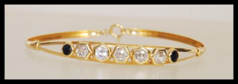 A stamped 750 18ct gold bangle bracelet set with five hexagonal cut white stones and two round cut