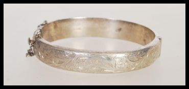 A hallmarked silver bangle bracelet having engraved scrolled detailing, with a hinged opening and