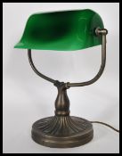 A vintage 20th century bankers desk lamp having an adjustable green glass shade raised on a brass