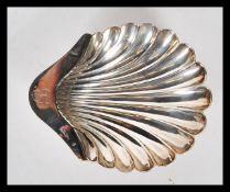 A silver hallmarked condiment dish in the form of a scallop shell being raised on three ball feet.