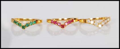 Three interlocking 18ct gold wishbone rings set with emeralds, rubies and diamonds. Unmarked but