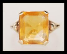 A 9ct gold dress ring, prong set with a square cut orange stone on a split shank mount. Unmarked but