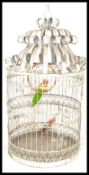 A 20th century large forged bird cage finished in white paint with two green and red  parrots  for