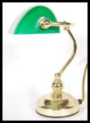A vintage 20th century bankers desk lamp having an adjustable green glass shade raised on a brass