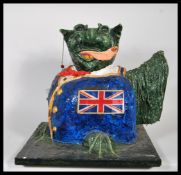 A paper mache figure of a gremlin/ winged gargoyle licking his lips, finished in dark green. Wearing