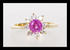 An unmarked 18ct gold ladies dress ring prong set with a round cut pink stone with a halo of white