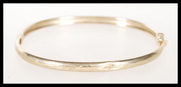 A stamped 375 9ct gold bangle bracelet with engraved decoration having a hinge opening. Weight 6.6g.
