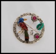A circular silver and enamel set brooch / pendant in the form of a tropical bird having floral