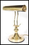 An Antique 20th Century style brass effect bankers lamp, having tubular shade and adjustable stem,