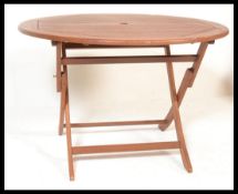 A contemporary teak wood outdoor garden table of circular form, raised on  a folding X-frame base