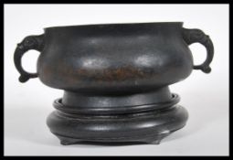 A Chinese bronze censer bowl of squat globular form with shaped twin handles, raised on a circular