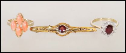 An early 20th Century bar brooch set with a round cut red stone to the centre having applied