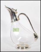 A 20th Century glass wine decanter of tilted form having silver white metal fixtures, being raised