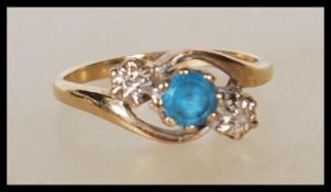 A stamped 9ct gold crossover ring set with a round cut blue topaz stone flanked by two illusion