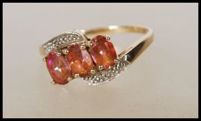 A stamped 375 9ct cross over gold ring set with three oval cut pink mystic topaz stones, having