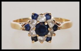 A hallmarked 9ct gold ring having a flower head set with blue and white stones. Hallmarked