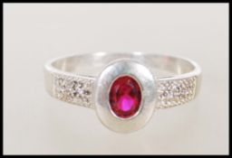 A ladies silver and cubic Zirconia ring. The silver rub over setting surrounding a coloured red
