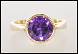 A hallmarked 18ct gold ladies dress ring bezel set with a round cut purple synthetic sapphire..