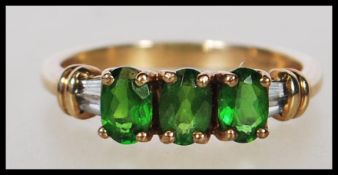 A hallmarked 9ct gold ring set with three oval cut green stones between white stone shoulders.