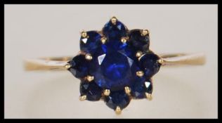 A hallmarked 9ct gold ring having a flower head of blue sapphires (synthetic). Hallmarked