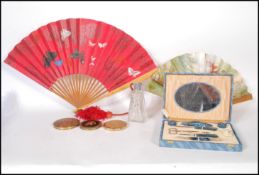 A group of three vintage compacts, all having floral decoration atop. Together with two fans one
