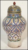 An early 20th Century polychrome Persian bulbous baluster lidded pot / olive jar, raised on