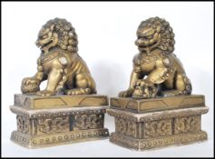 A pair of gilt temple dogs / foo dogs, both posed upon pedestal bases with their paws upon a