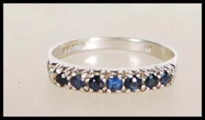 A hallmarked 9ct white gold ring set with a row of round cut blue stones. Hallmarked London 1976.