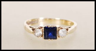 A hallmarked 9ct gold ring set with a square cut blue stone flanked by two round cut white stones.
