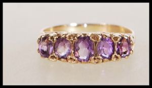 A hallmarked 9ct gold ring set with five oval cut amethyst in a scrolled decorative setting.