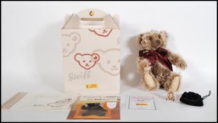 A boxed Steiff teddy bear titled 'The Million Hugs Bear' in copper brown wearing a burgundy scarf