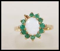 A hallmarked 9ct gold ring set with a central opal cabochon with a halo of green stones.