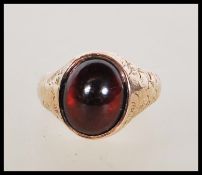 A hallmarked 15ct gold ring set with a red garnet cabochon, having engraved shank and shoulders.