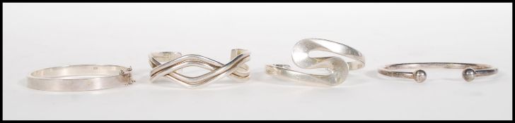 A group of four stamped 925 silver bangle bracelet to include a cross over design bangle, a curved